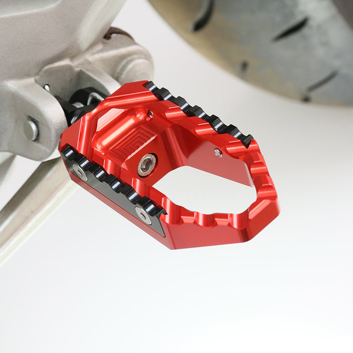 Rear black touring wide foot pegs for Aprilia RSV1000 Tuono V4R TRC by MC Motoparts, shown installed on motorcycle.